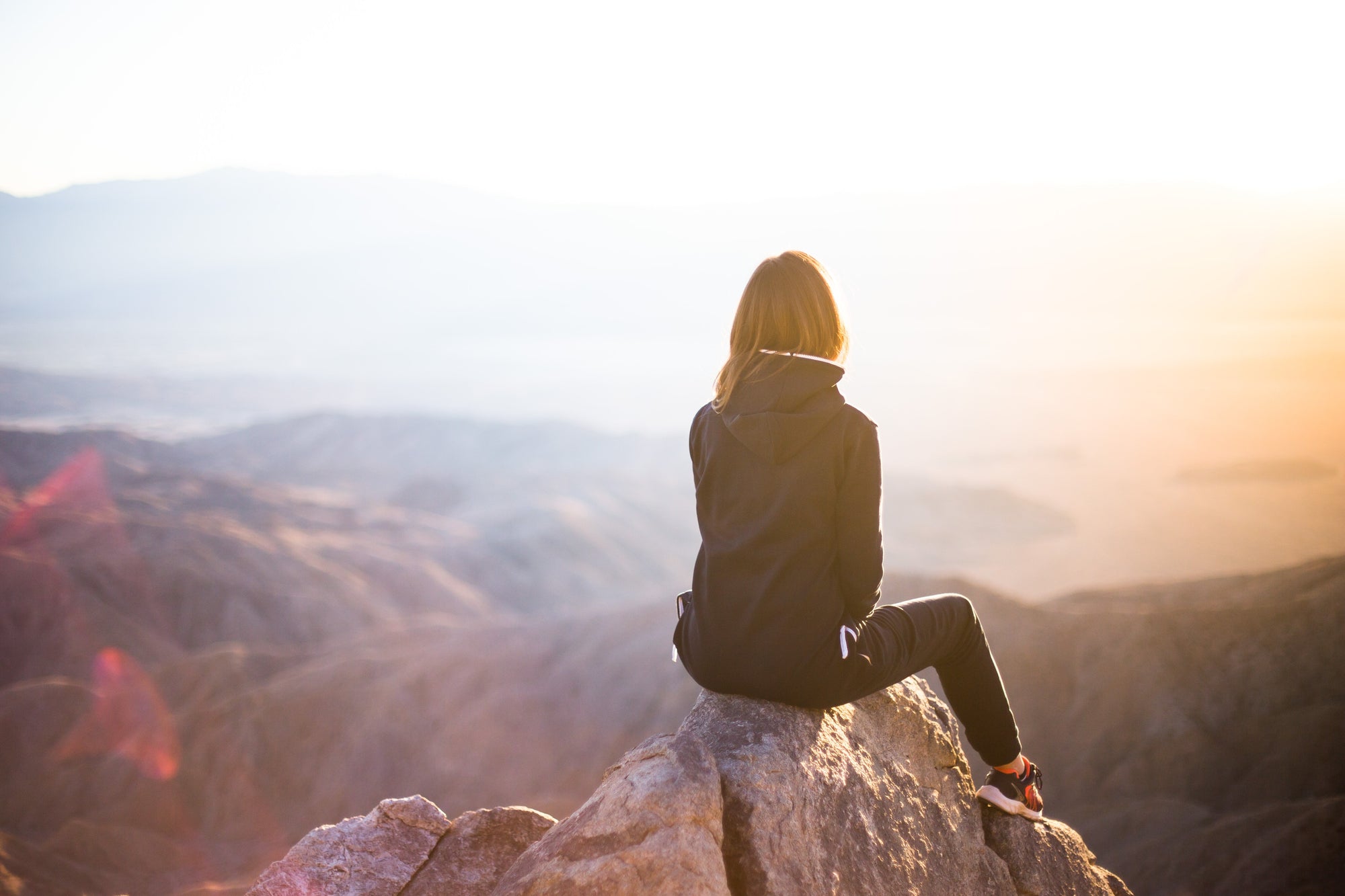 woman sitting on a top of a mountain watching sunset feeding mental wellbeing